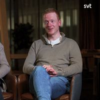 Två personer sitter i fåtöljer i en studio med dämpad belysning.