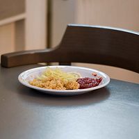 Delad bild. Till vänster, en elev. Till höger. En tallrik med mat står på ett bord där stolen hänger på bordet.