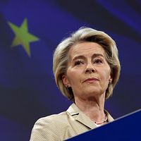 Kvinna vid talarstol framför EU-flagga med två synliga stjärnor i bakgrunden.