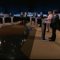 Åtta partiledare står vid podium i en tv-studio inför en partiledardebatt.
