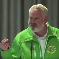 Delad bild. Till vänster talar en kvinna vid mikrofon. Till höger man i grön jacka vid talarstol.