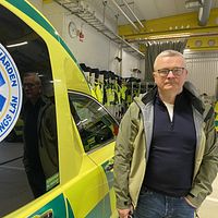 Anders Ingvarsson står bredvid en ambulans från Region Jönköpings län. Han tittar allvarligt in i kameran.