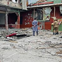 Två personer inspekterar raserade rester efter en explosion i ett kraftigt skadat hus.