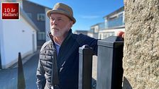 Man i hatt framför hus på solig dag. Text: ”10 år Halland” i hörnet.