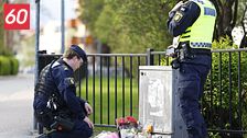 Två poliser vid ett minnesmärke med blommor på trottoar nära ett staket.