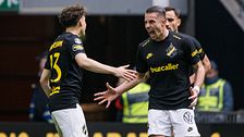 Två AIK-spelare på fotbollsplan med sträckta händer, publik och vakter i bakgrunden.