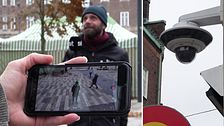 En reporter från SVT står på ett torg och filmas samtidigt av en övervakningskamera som syns i en mobiltelefon i förgrunden.