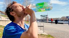 Daniel Brunell sitter på strandpromenaden och dricker vatten ur en flaska.