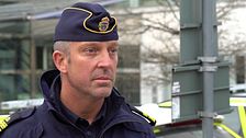 Henrik Dahlström i uniform vid en gata, med polisbilar i bakgrunden.