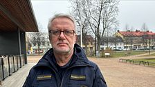 Polis i uniform står framför en parkmiljö med bostadshus i bakgrunden.