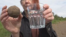 Kvinna visar en potatis och ett glas vatten på en gård