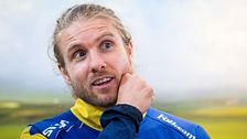 Person i gul-blå sporttröja står utomhus med landskap i bakgrunden.