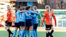 Fotbollslag i blåa tröjor firar på planen, motståndare i orangea tröjor syns i bakgrunden.