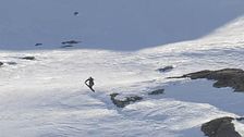 Ensam skidåkare åker nerför en snötäckt bergssida med klippor och skuggor.