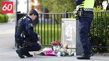 Två poliser vid ett blomhav på trottoaren, minnesplats efter händelse utomhus.