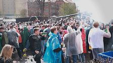 Stor folkmassa i regnponchos samlas utomhus för fest eller demonstration i stadsmiljö.
