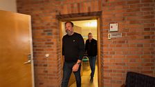 Två män går genom en dörröppning i en byggnad med tegelväggar.
