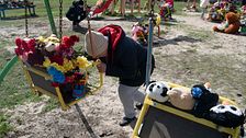 Bilden föreställer en sörjande person i Ukraina vid en gunga som är fylld med blommor