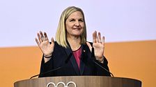 Kvinna talar vid olympisk podium med höjda händer.