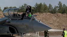 Pilot kliver ur ett militärflygplan på en flygbas, personal står bredvid.