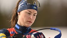 Skidskytt siktar med gevär under tävling, iklädd tävlingsdräkt och pannband.