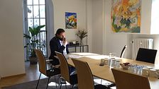En man läser ett papper i ett soligt kontorsrum med konferensbord och konst på väggarna.