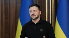 Person håller tal framför ukrainska flaggor och håller ett papper i handen.