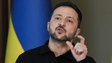 Volodymir Zelenskyj gestikulerar framför Ukraina-flaggor.