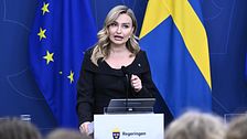 Ebba Busch vid talarpodium med Sveriges och EU:s flaggor i bakgrunden.