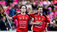 Två innebandyspelare i röda matchtröjor firar tillsammans på planen under en match.