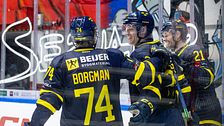 Tre ishockeyspelare firar ett mål framför sarg med reklamskyltar.