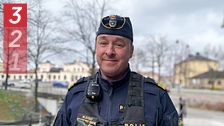Polis med uniform och utrustning i stadsmiljö. Bakgrund med park och byggnader.