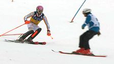 Två skidåkare svänger runt en port på en snötäckt slalombana.