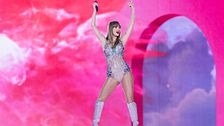 Taylor Swift med armarna i luften mot en rosa bakgrund