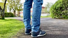 Person i jeans och sneakers står på en asfalterad gångväg i grönskande parkmiljö.