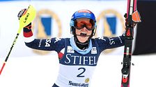Alpin skidåkare med nummer två firar med uppsträckta armar, hållandes stavar och skidor.