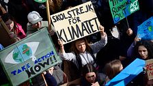 Greta Thunberg står i ett hav av demonstrater, hållandes ett plakat där det står ”Skolstrejk för klimatet”
