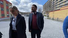 Personer promenerar bredvid byggnader, en återspeglar en blå himmel med moln.