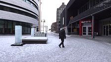 En man går genom en snötäckt gata mellan moderna byggnader.