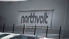 Northvolt-logga på fabriksbyggnad med bilar i förgrunden.