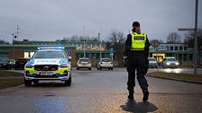 Polis stoppar trafik vid väg med polisbil och flera bilar i bakgrunden.