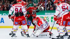 Hockeyspelare kämpar om pucken framför målvakten i en intensiv match.