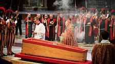 Kista omgiven av präster och vakter vid en ceremoni i en kyrka.