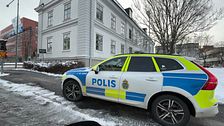 Polisbil parkerad utanför en herrgårdslik byggnad på en snötäckt gata.