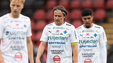 Tre fotbollsspelare i vita matchställ på planen.