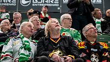 Rolf Lassgård och flera andra Brynässupportrar i klubbtröjor sitter på läktaren under en match.