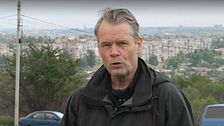 Person utomhus med stad och parkerade bilar i bakgrunden.