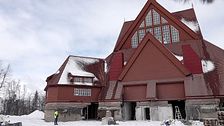En person med gul varselväst ser väldigt liten utan medan han tittar upp mot den väldiga och röda träkyrkan i Kiruna.