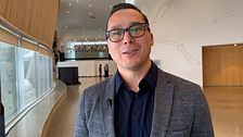 Man i grå kavaj står i ett modernt rum med stora fönster och trägolv.