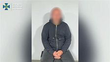 En man med blurrat ansikte sitter på en stol med knäppta händer framför en vit vägg. Bilden kommer från Ukrainska SBU via Telegram.